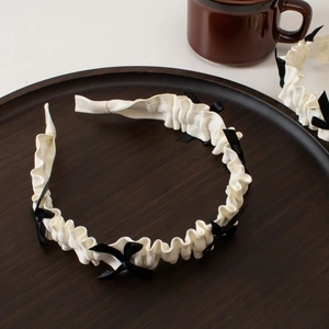 Detailed top view of a white pleated Lolita headband with black satin bows on a tray