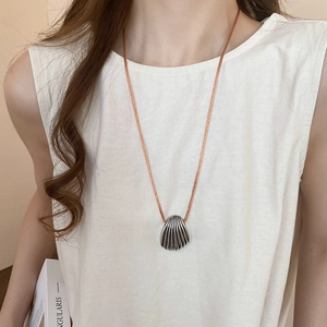 Close-up of silver shell pendant with textured grooves on a brown cord necklace