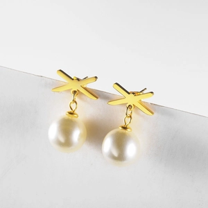 Close-up of golden X-shaped earrings with white pearl pendants on textured display