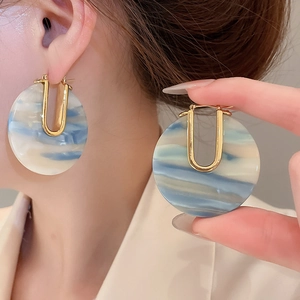 Détail de boucles d'oreilles dorées en U avec disques en acrylique marbré bleu