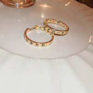Elegant gold hoop earrings with colorful zircon heart charms on a white ceramic plate