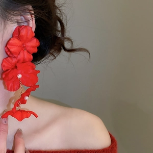 Close-up of elegant red fabric flower earrings with pearls worn by a female model