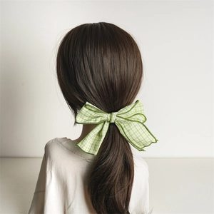 Green plaid fabric bow hair clip shown from behind on a high ponytail for girls