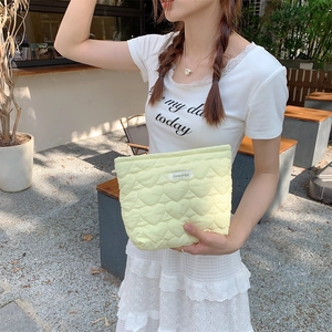 Detailed view of yellow quilted heart pattern clutch bag held outdoors by model