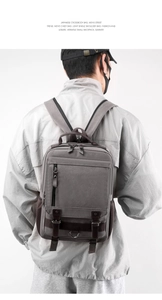Rear view of model wearing a compact dark gray canvas backpack with premium leather accents