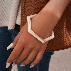 Detail of marble pattern resin hexagonal bangle worn with a woven bag accessory
