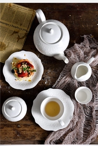 Top view of European white ceramic tea set with embossed patterns on dark wood table