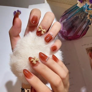 Amber gradient press-on nails with 3D bows and pearls on a warm cozy background