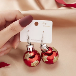 Detail of red Christmas bulb earrings with gold glitter stars on champagne velvet