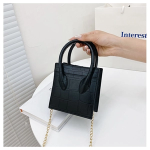 Detail of a black crocodile pattern handbag with gold chain strap on a white table