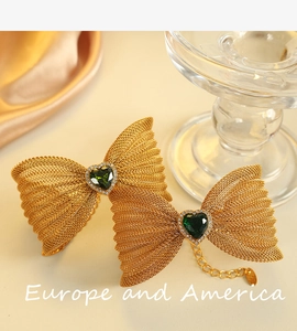 Close-up of golden mesh bow bracelet with green heart gemstone on luxury satin