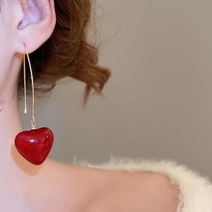 Close-up of red heart pendant earrings with long gold chain hooks worn by a model