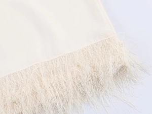 Detail of elegant cream-white top showing fine fabric texture and long fringe tassels