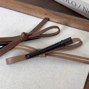 Detailed macro view of brown leather bow hair clips on minimalist fabric background