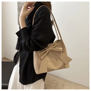 Detail of a beige PU leather shoulder bag with a large bow decoration and slim strap
