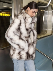 Detail of high neck faux fur coat in black spotted white pattern on subway