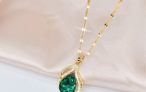 Macro shot of gold waterdrop necklace with green gemstone on soft pink silk fabric