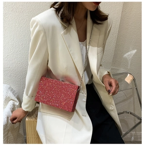 Close-up of red glitter rectangular clutch with silver metal chain on white blazer