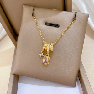 Detail of gold titanium necklace with pink rectangular gemstone and pavé rings in a box