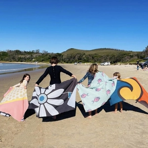 Quick-dry microfiber beach towel with daisy and wave prints shown in a sunny seaside setting