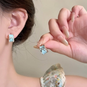 Macro detail of light blue enamel bow stud earrings with silver bow accent on ear