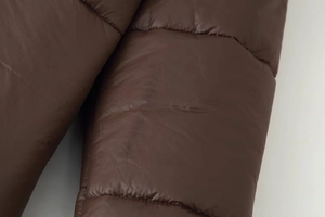 Gros plan de la manche d'une veste matelassée marron foncé montrant la texture lisse