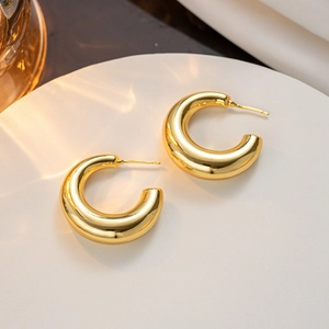 Polished gold thick C-shaped hoop earrings on a white minimalist display tray