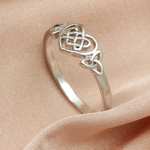 Macro detail of silver heart-shaped Celtic knot ring on soft silk background