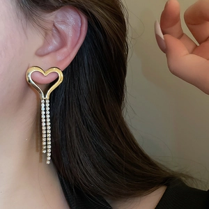 Close-up of heart-shaped earrings with long rhinestone tassels on woman's ear