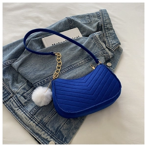 Détail du sac en velours bleu matelassé avec chaîne dorée et pompon en fourrure blanche