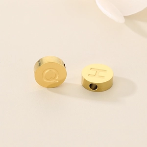 Detailed macro view of gold stainless steel flat round beads with engraved letters Q and H