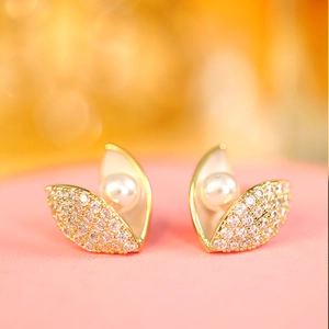 Detailed view of gold shell earrings with micro-pave zircons and white pearl inlay