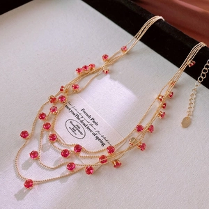 Close-up of layered gold chain necklace featuring elegant red gemstone charms on card