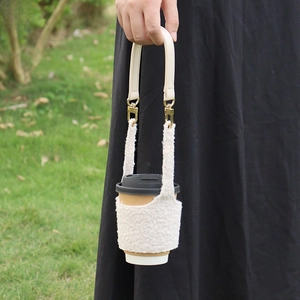 Detail of soft white lamb wool coffee cup sleeve with cream faux leather handle and gold clips