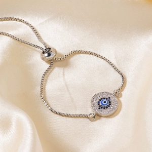 Classic silver Evil Eye adjustable bracelet with blue sparkling crystals on silk background