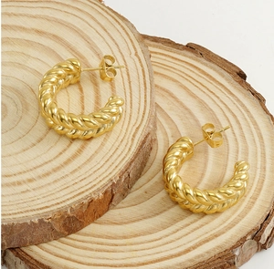 Close-up of gold twisted croissant hoop earrings resting on natural wooden pieces