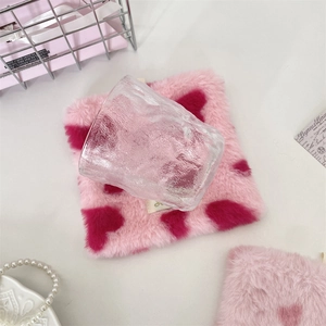 Detail of pink plush heart coaster with hammer-textured glass cup on minimalist desk