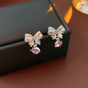 Detailed macro view of silver bow earrings with colorful rhinestones and purple drop gems