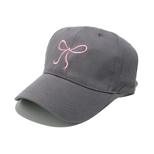 Close-up of pink ribbon bow embroidery on dark gray cotton twill baseball cap fabric