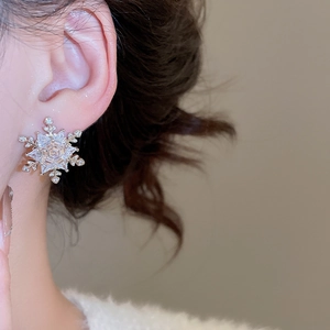 Macro close-up of a silver snowflake stud earring with cubic zirconia on a model ear