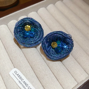 Detailed view of woven blue floral earrings with yellow crystals on a display tray