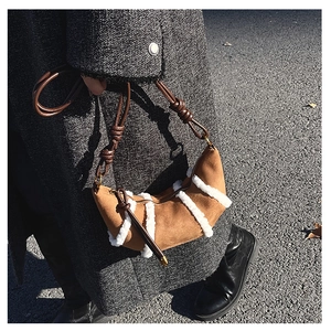 Close-up of suede croissant bag with white fleece stripes worn over a grey wool coat