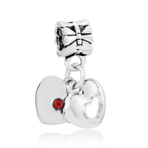 Close-up of silver heart charms with red zircon and bow connector on white background
