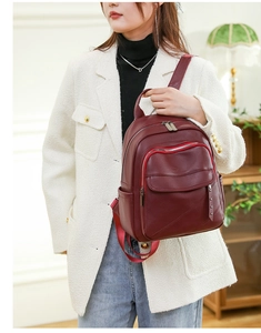 Detailed close-up of burgundy lychee leather backpack with metal rivets and zipper pockets