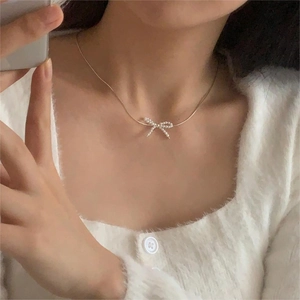 Detail shot of a delicate golden bow necklace with pearl inlays worn with a white sweater