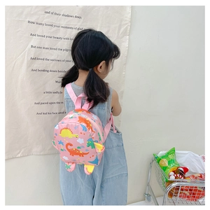 Detailed view of pink toddler backpack featuring colorful cartoon dinosaurs on a child model