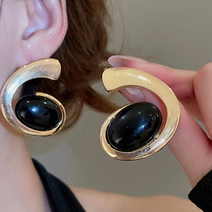 Close-up of vintage style gold C-shape earrings featuring large black oval resin stones