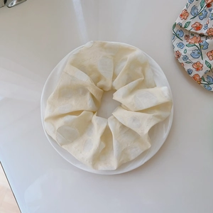 Detail of a large cream ruffled hair scrunchie with white polka dots on a white ceramic plate