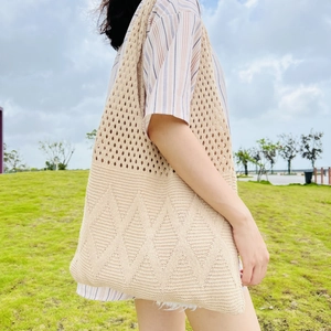 Beige knitted tote bag with geometric pattern shown outdoors on a sunny grass field