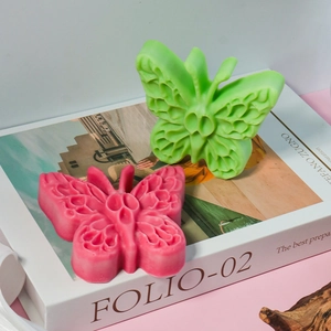 Dettaglio degli stampi in silicone a farfalla traforata in rosa e verde su un libro
